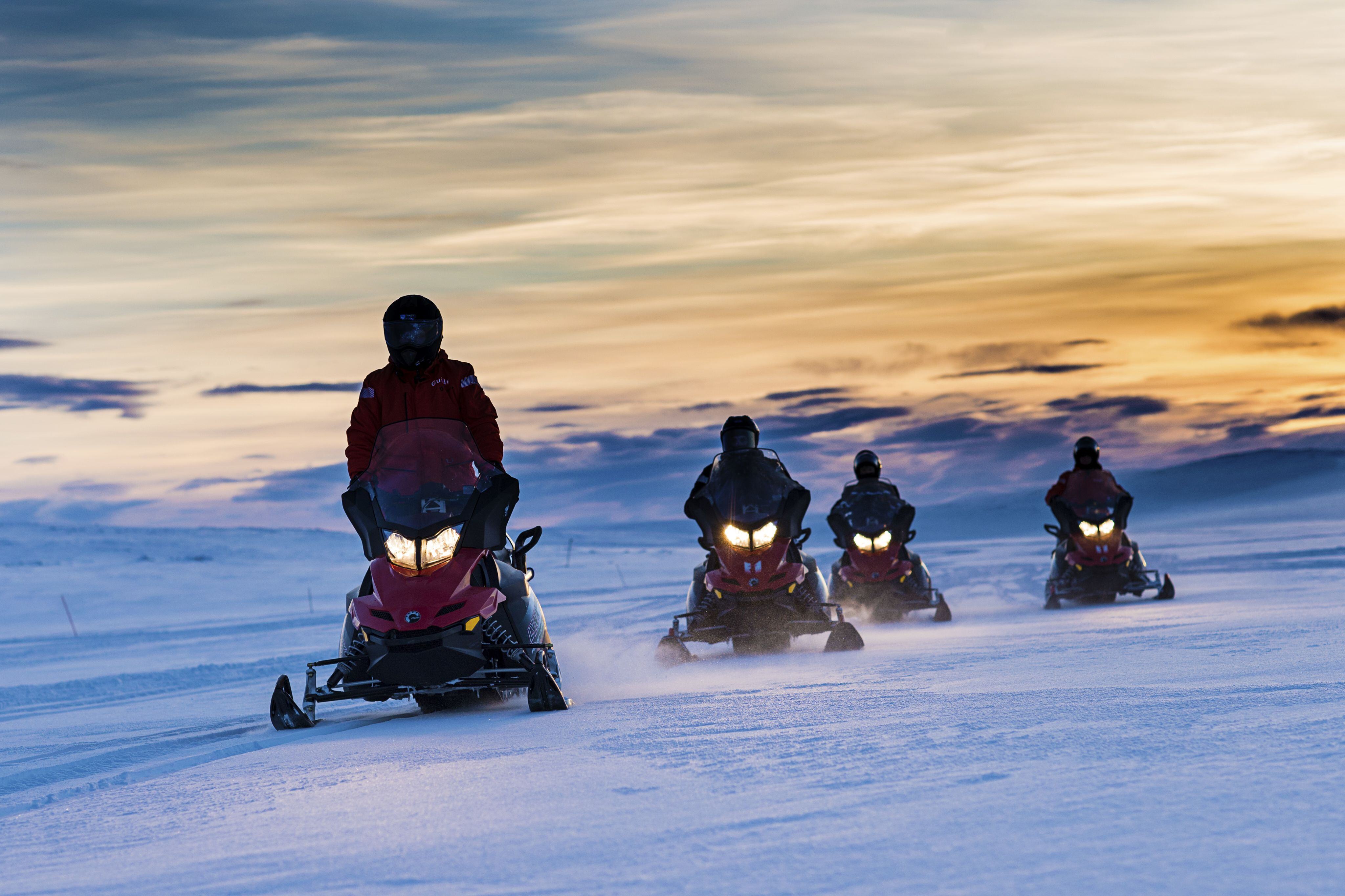 Snowmobiles driving in the sunset